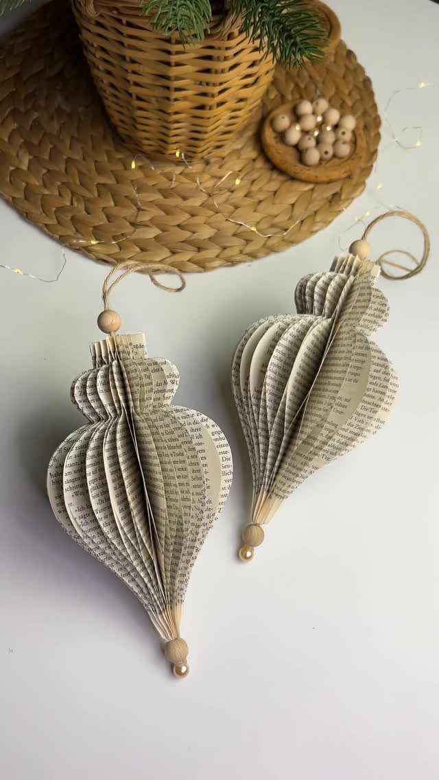 Two teardrop-shaped ornaments crafted from pleated book pages resting on a white surface.