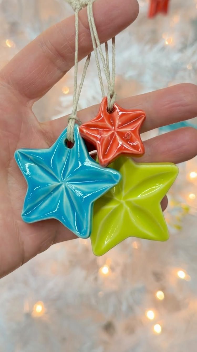 Hand holding three colorful, glossy star-shaped ceramic ornaments with white hanging strings.