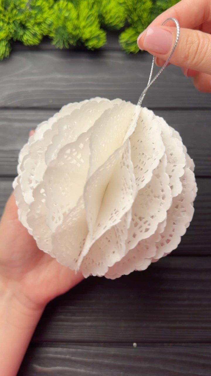 Hands holding a white spherical ornament made from layered decorative lace paper patterns.