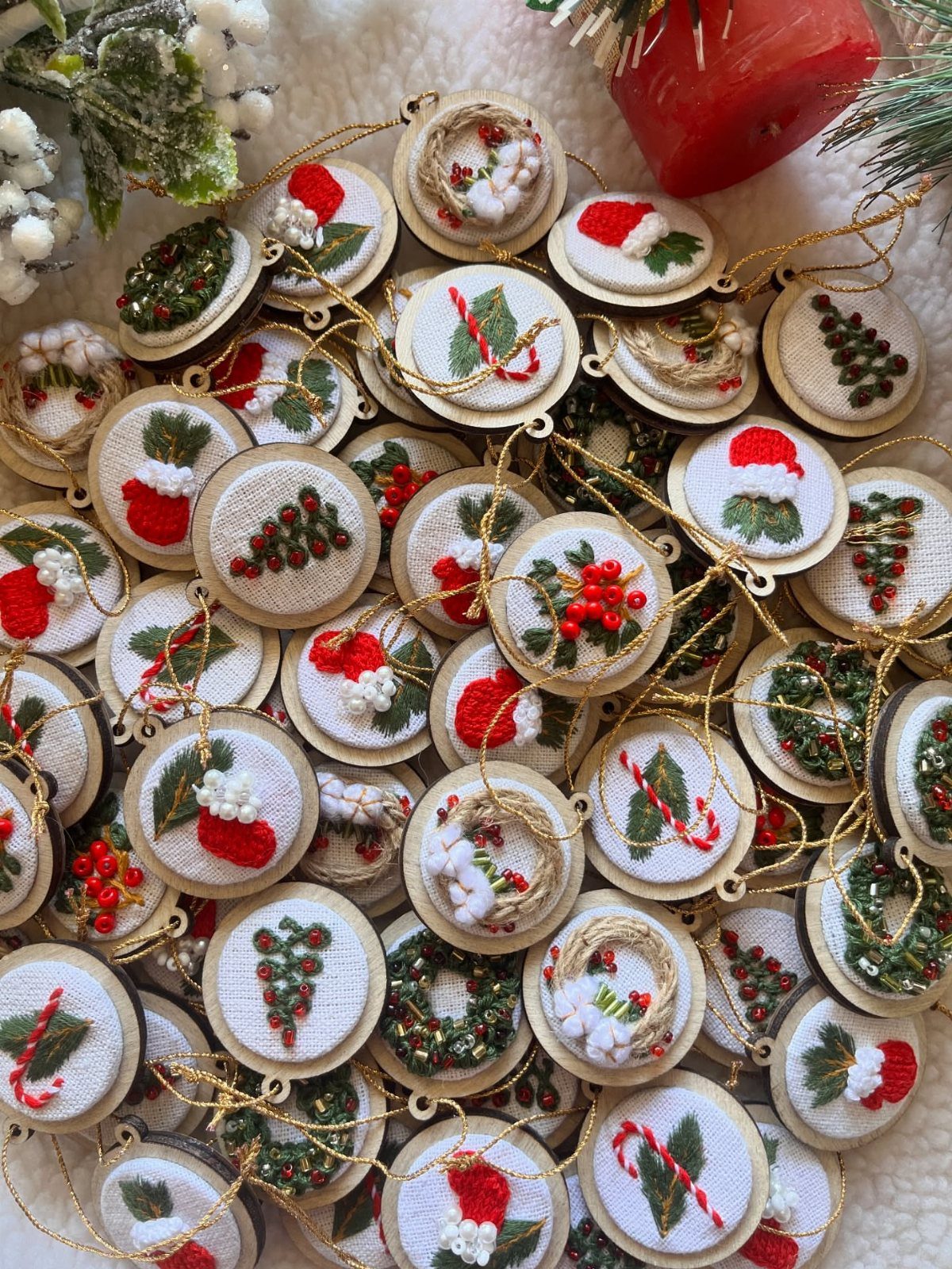 Numerous small, hand-embroidered fabric ornaments with festive holiday patterns hanging in a group.