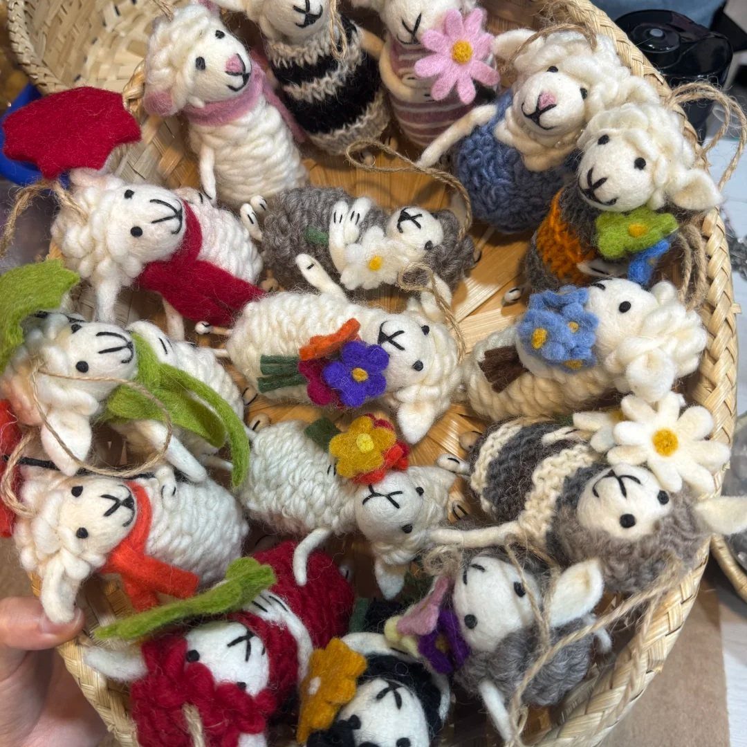 Handmade needle felted wool sheep ornaments with colorful tiny clothes and flowers in a basket.