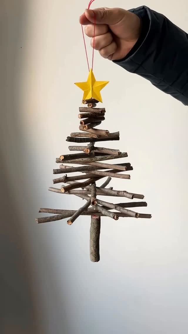 A hand holding a handmade Christmas tree ornament made of small twigs with a yellow star.
