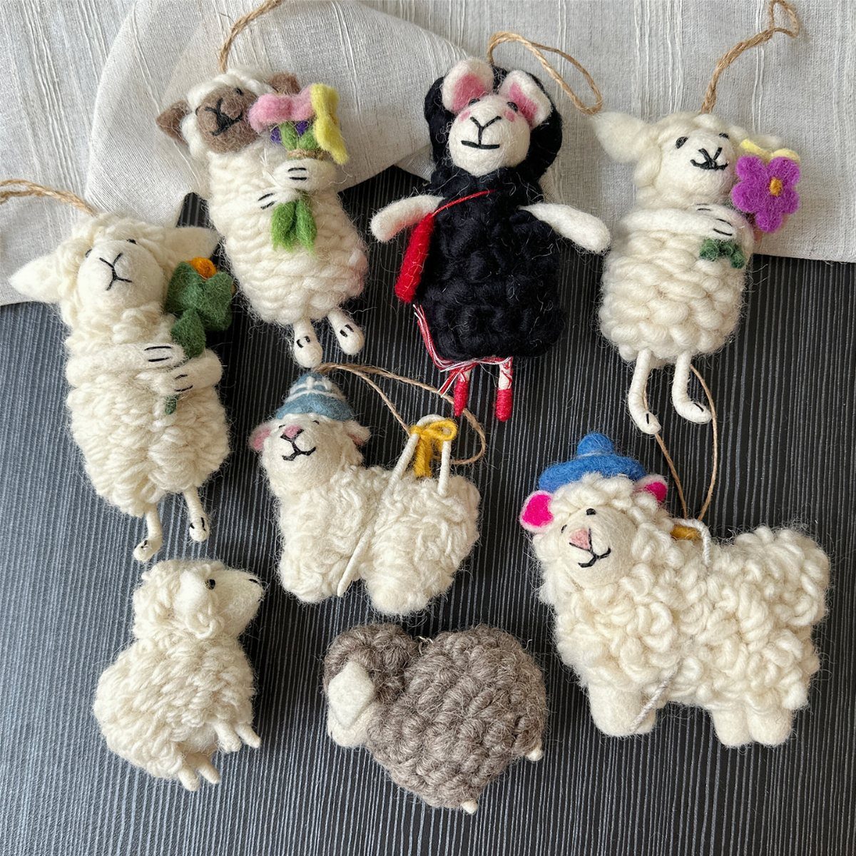 Handmade yarn sheep ornaments in various colors and styles arranged on a dark surface.