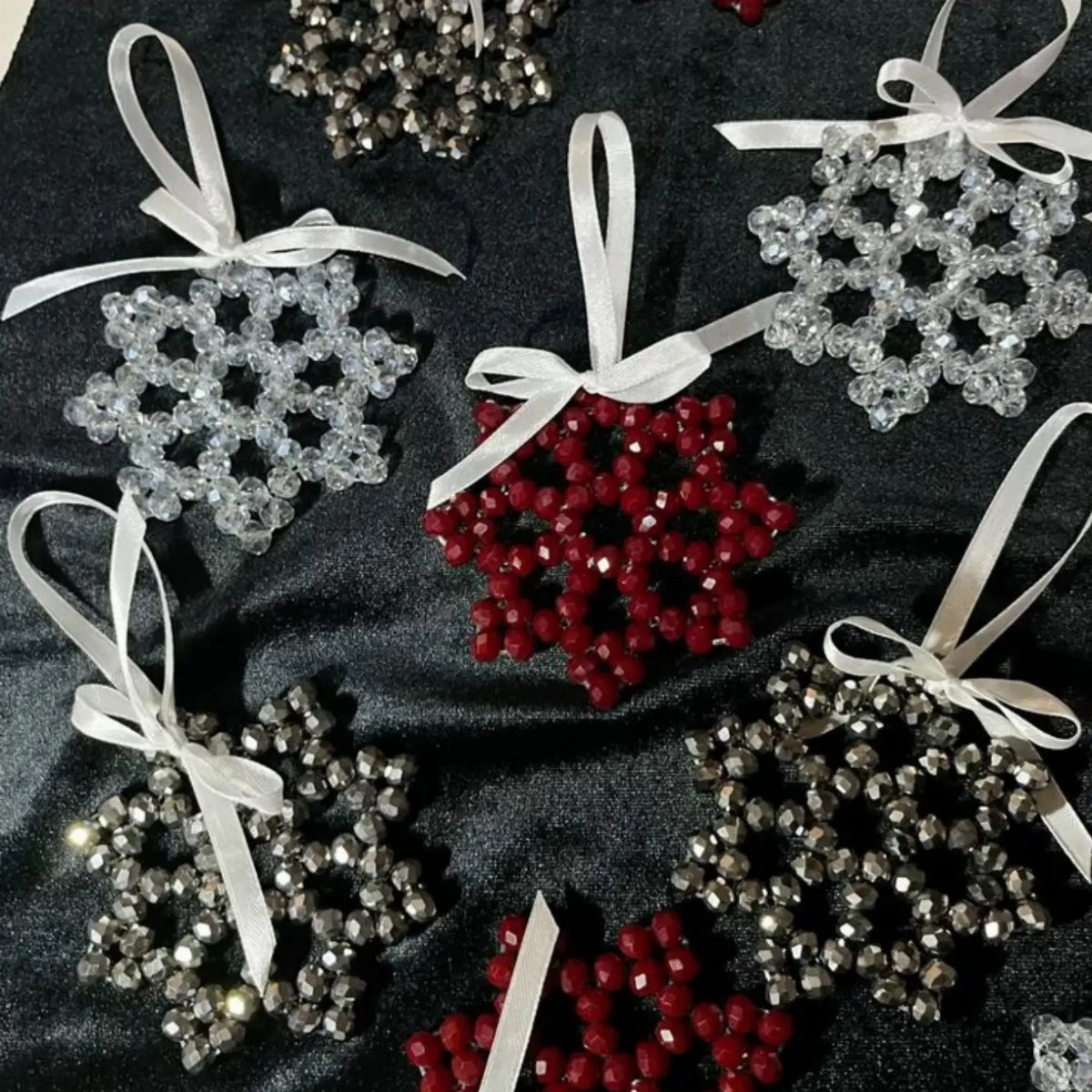 26 Handmade Ornaments: DIY Projects from Paper to Pinecones 22 Beaded snowflake ornaments in silver, white, and red colors with white satin ribbons on dark fabric.