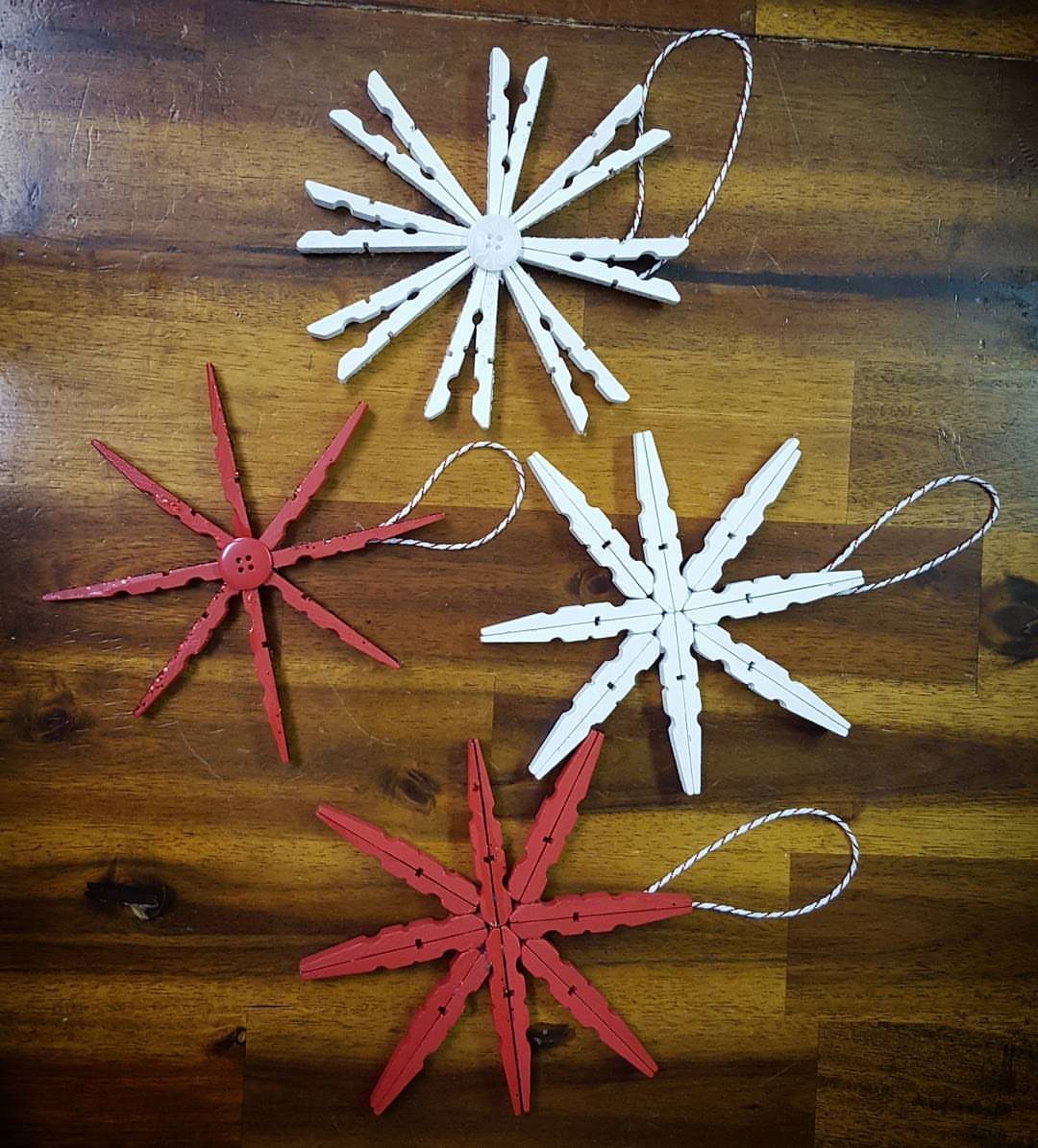 26 Handmade Ornaments: DIY Projects from Paper to Pinecones 2 Four clothespin snowflake ornaments in red and white resting on a wooden table.