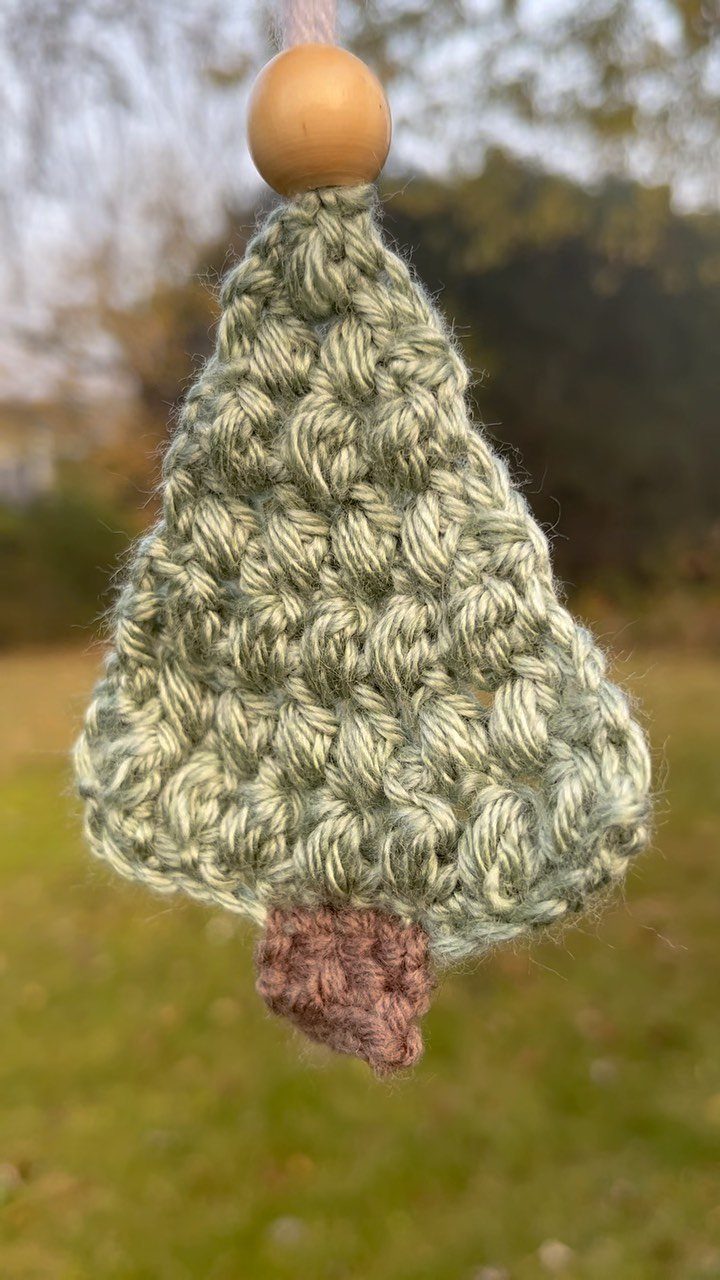 26 Handmade Ornaments: DIY Projects from Paper to Pinecones 24 A sage green crocheted Christmas tree ornament with a wooden bead hanging outdoors.