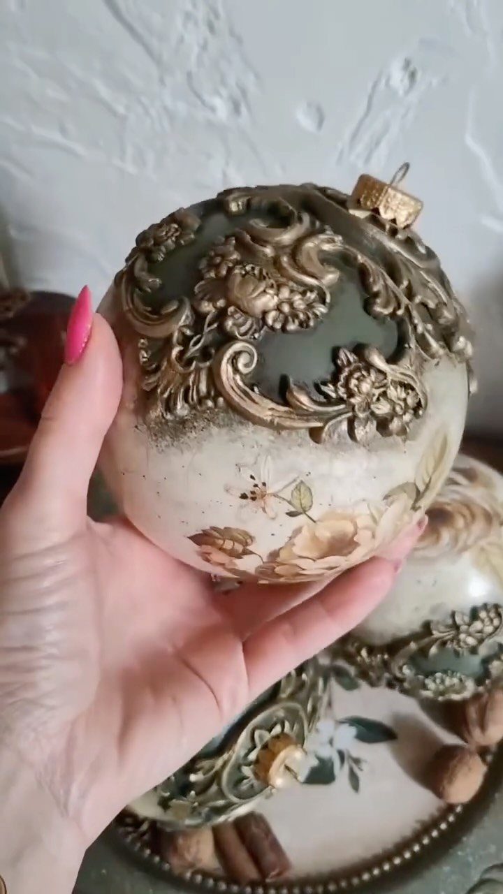 26 Handmade Ornaments: DIY Projects from Paper to Pinecones 14 Hand holding a decorative Christmas ornament with gold relief and floral decoupage patterns.