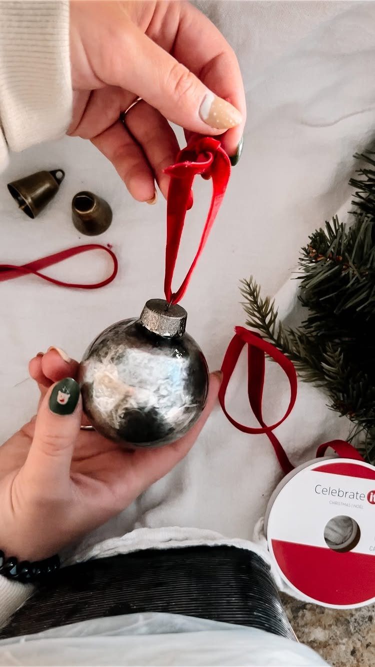 26 Handmade Ornaments: DIY Projects from Paper to Pinecones 19 Hands holding a silver mercury glass Christmas ornament with a red velvet ribbon.