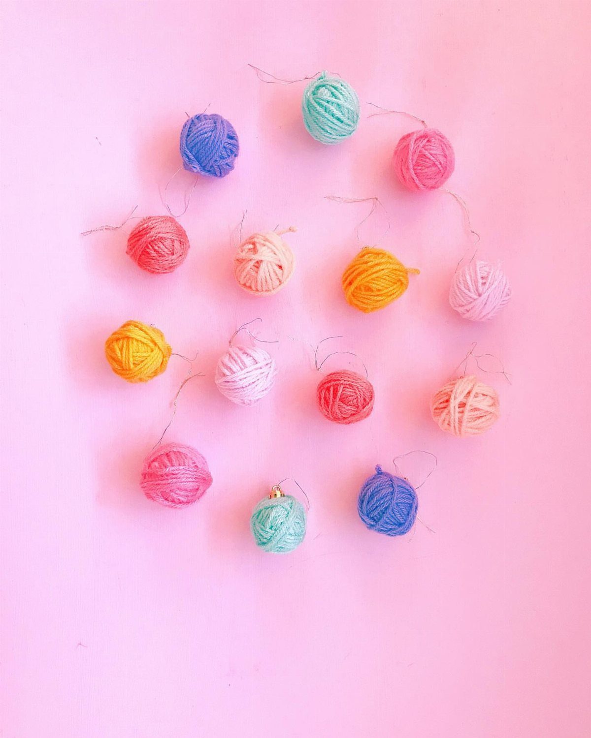 26 Handmade Ornaments: DIY Projects from Paper to Pinecones 12 Colorful yarn ball ornaments arranged in a circle on a bright pink background.