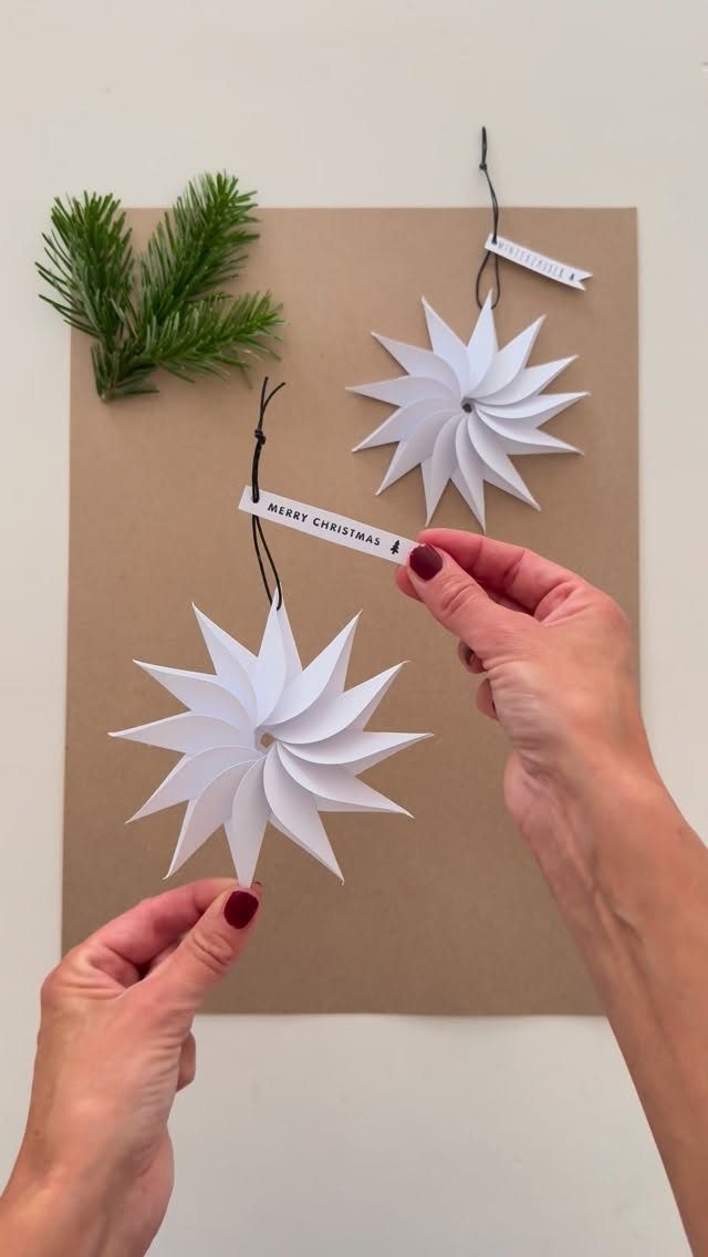 26 Handmade Ornaments: DIY Projects from Paper to Pinecones 1 Two white paper star ornaments being held by hands over a brown paper background.