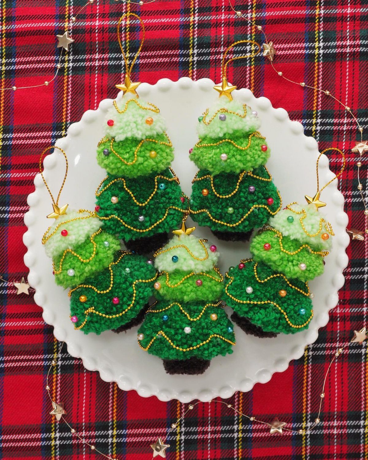 26 Handmade Ornaments: DIY Projects from Paper to Pinecones 15 Five green pom-pom Christmas tree ornaments decorated with gold beads on a white plate.