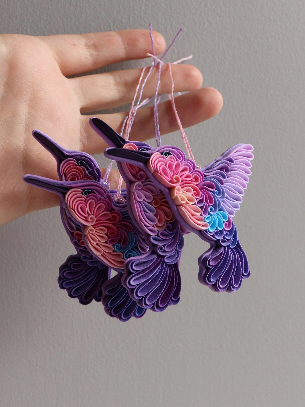 26 Handmade Ornaments: DIY Projects from Paper to Pinecones 25 Two colorful quilled paper hummingbird ornaments held by a hand against a grey background.