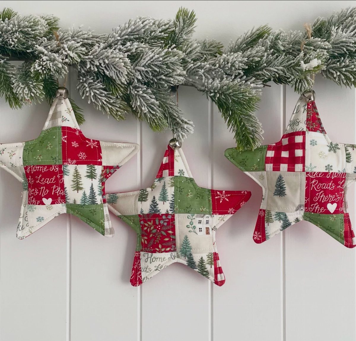26 Handmade Ornaments: DIY Projects from Paper to Pinecones 13 Three star-shaped quilted fabric ornaments hanging from a frosted evergreen garland against white wood paneling.