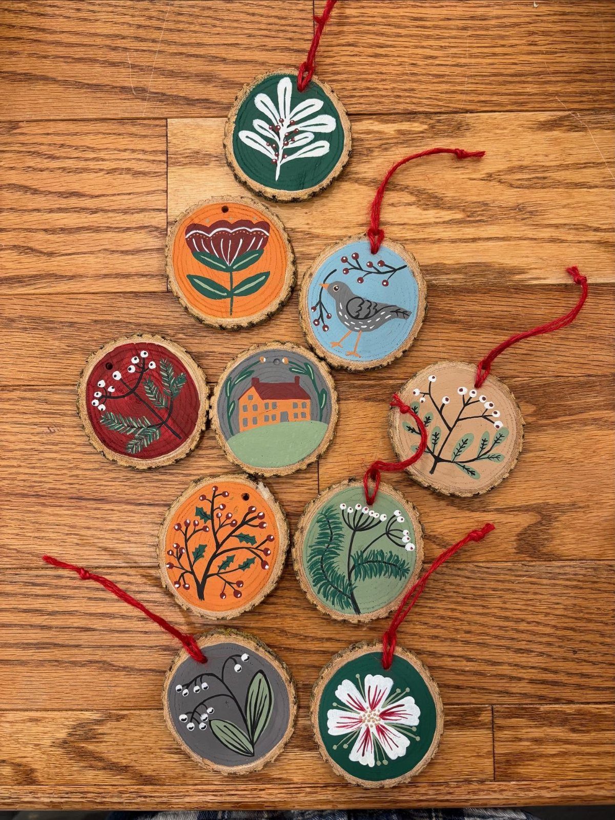 26 Handmade Ornaments: DIY Projects from Paper to Pinecones 7 Ten painted wood slice ornaments with various nature designs lying on a wooden table.