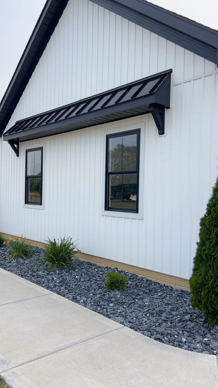 11 Inexpensive Landscaping Ideas for a Better Yard 9 Dark grey crushed stone landscaping bed with small green plants along a white house wall.