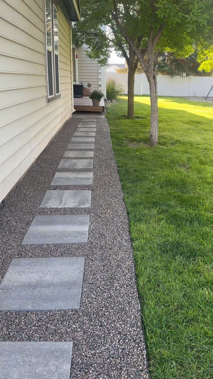 11 Inexpensive Landscaping Ideas for a Better Yard 4 Grey stone pavers set in gravel create a walkway alongside a house and green lawn.