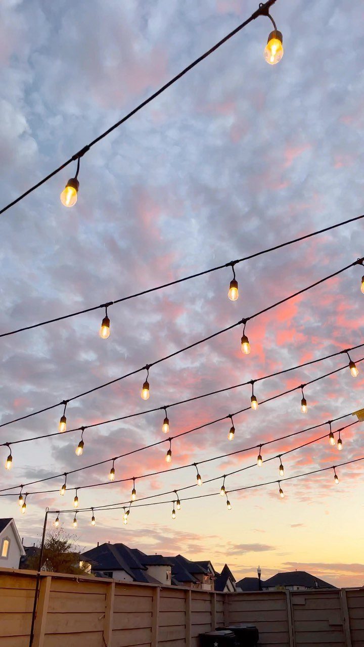 11 Inexpensive Landscaping Ideas for a Better Yard 10 String lights glow against a colorful sunset sky above a wooden backyard fence.