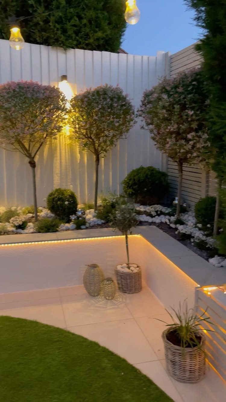 11 Inexpensive Landscaping Ideas for a Better Yard 2 Warm LED light strips illuminating a modern backyard patio with manicured trees and white garden beds.