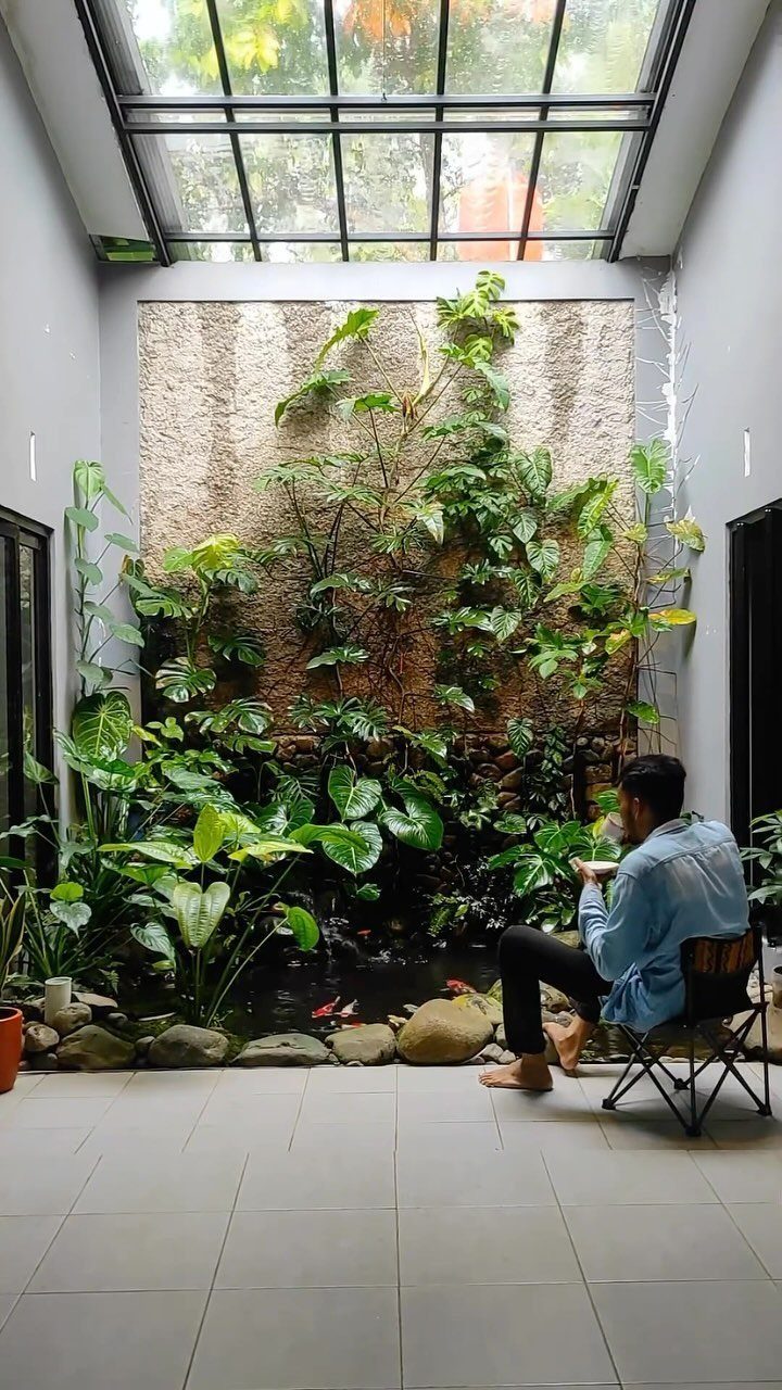 Interesting Garden Ideas: 9 Spaces That Pull You In 9 A man sitting in a chair facing a lush vertical garden wall under a glass skylight.