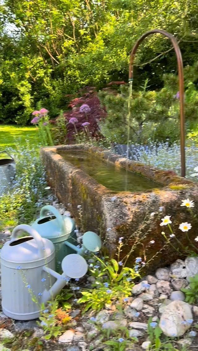 Interesting Garden Ideas: 9 Spaces That Pull You In 8 A stone water trough with a copper pipe pouring water amidst wildflowers and watering cans.