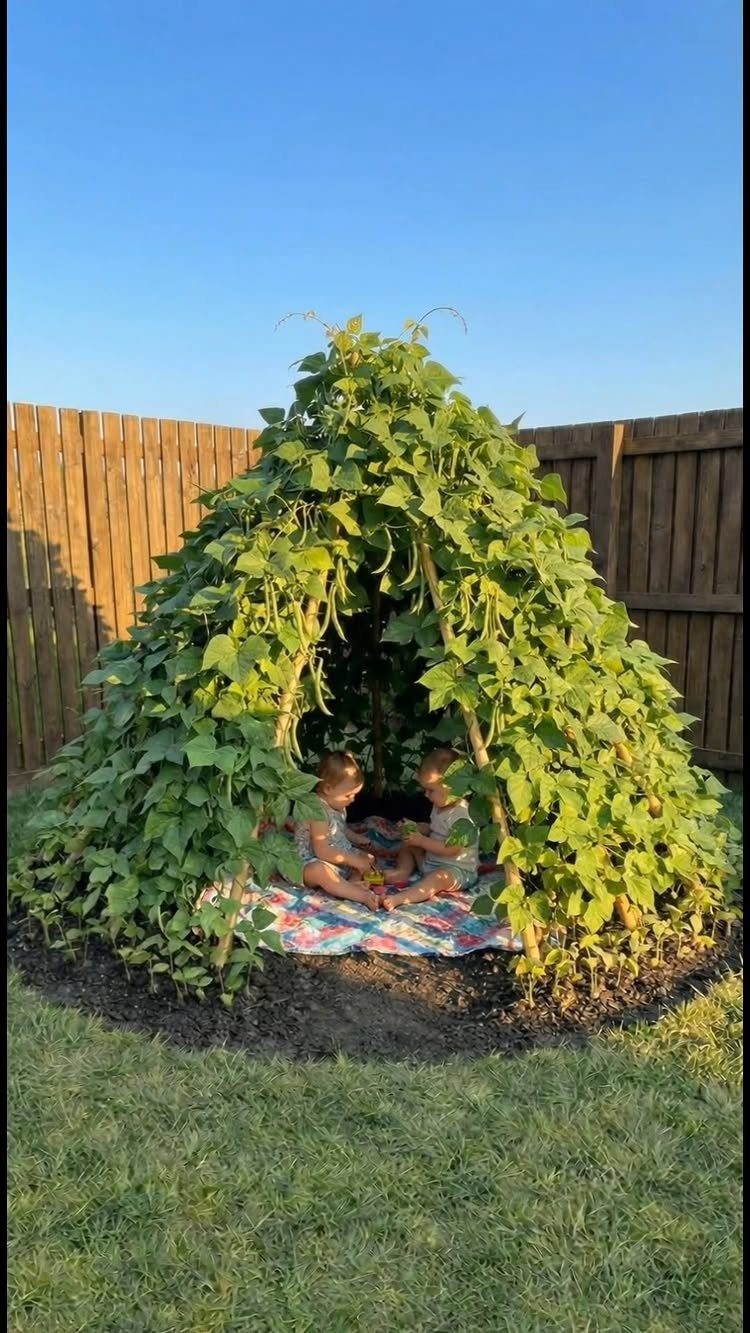 Interesting Garden Ideas: 9 Spaces That Pull You In 3 Two children sitting on a blanket inside a large green bean plant teepee structure.