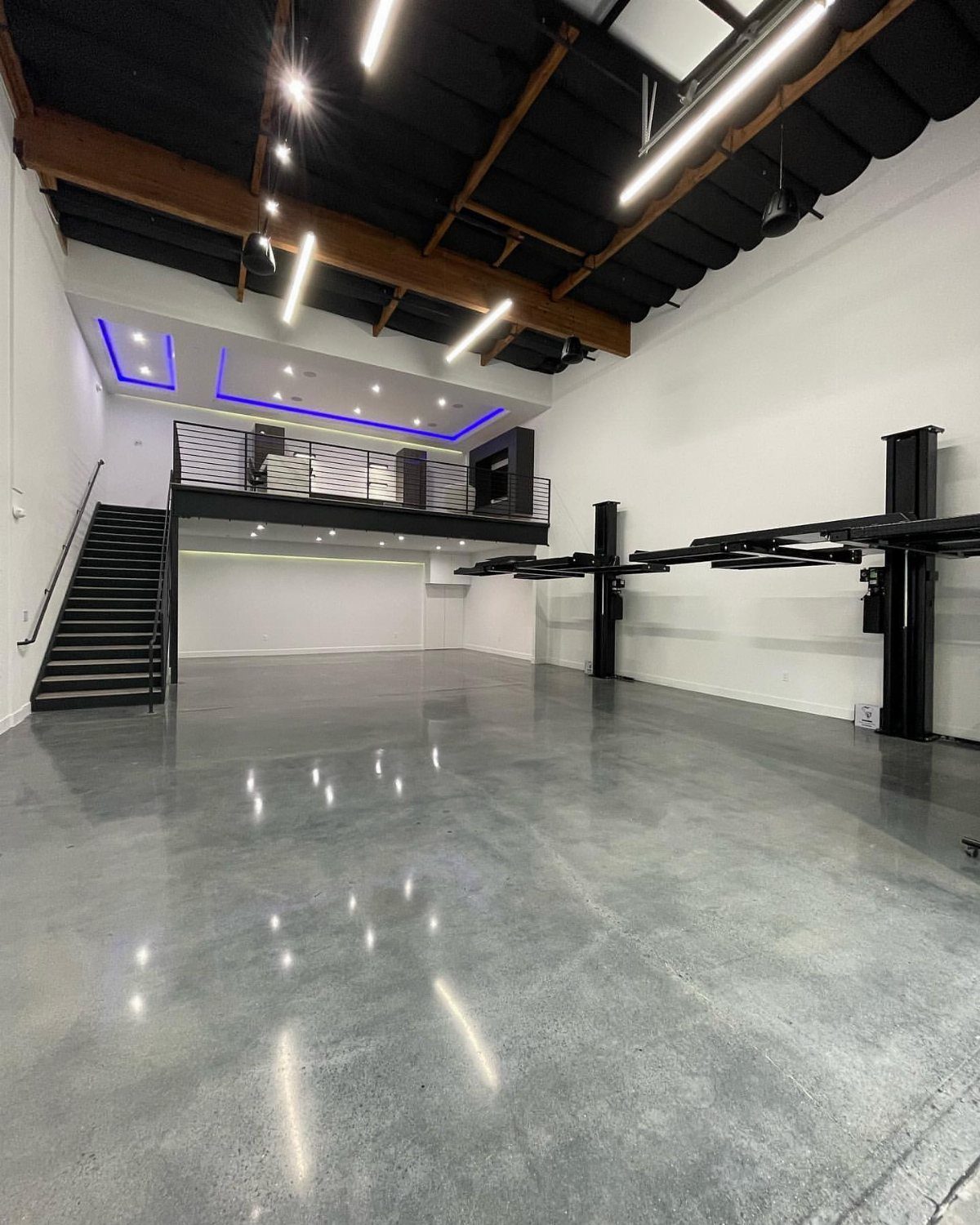 A large modern garage with polished concrete floors and a black mezzanine loft level.