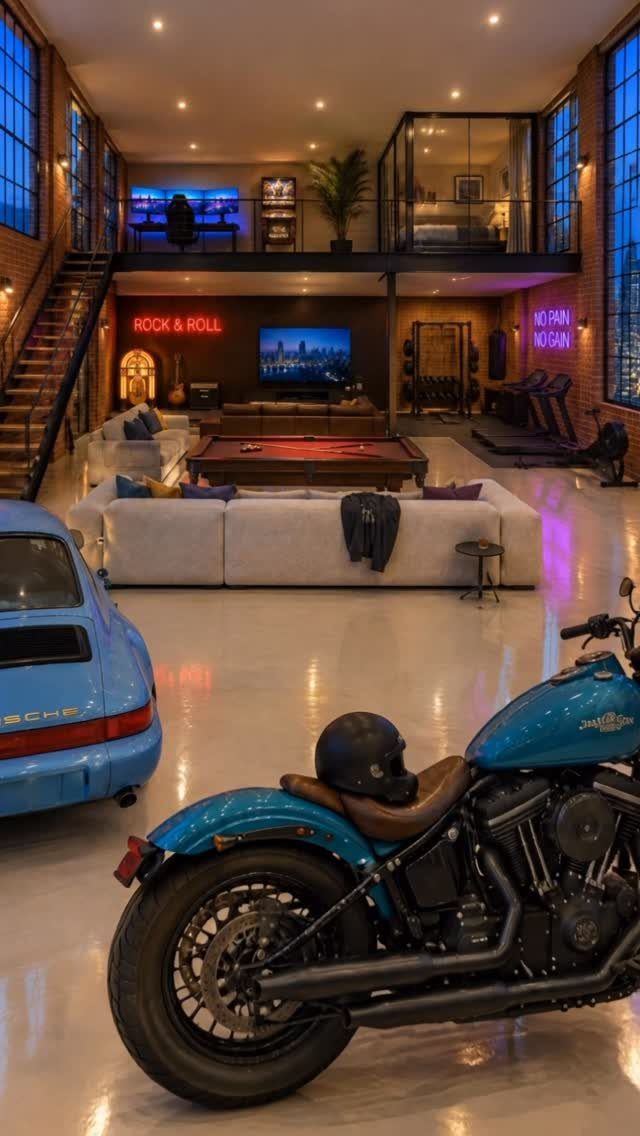 A blue motorcycle and car parked in a large industrial garage loft with exposed brick walls.