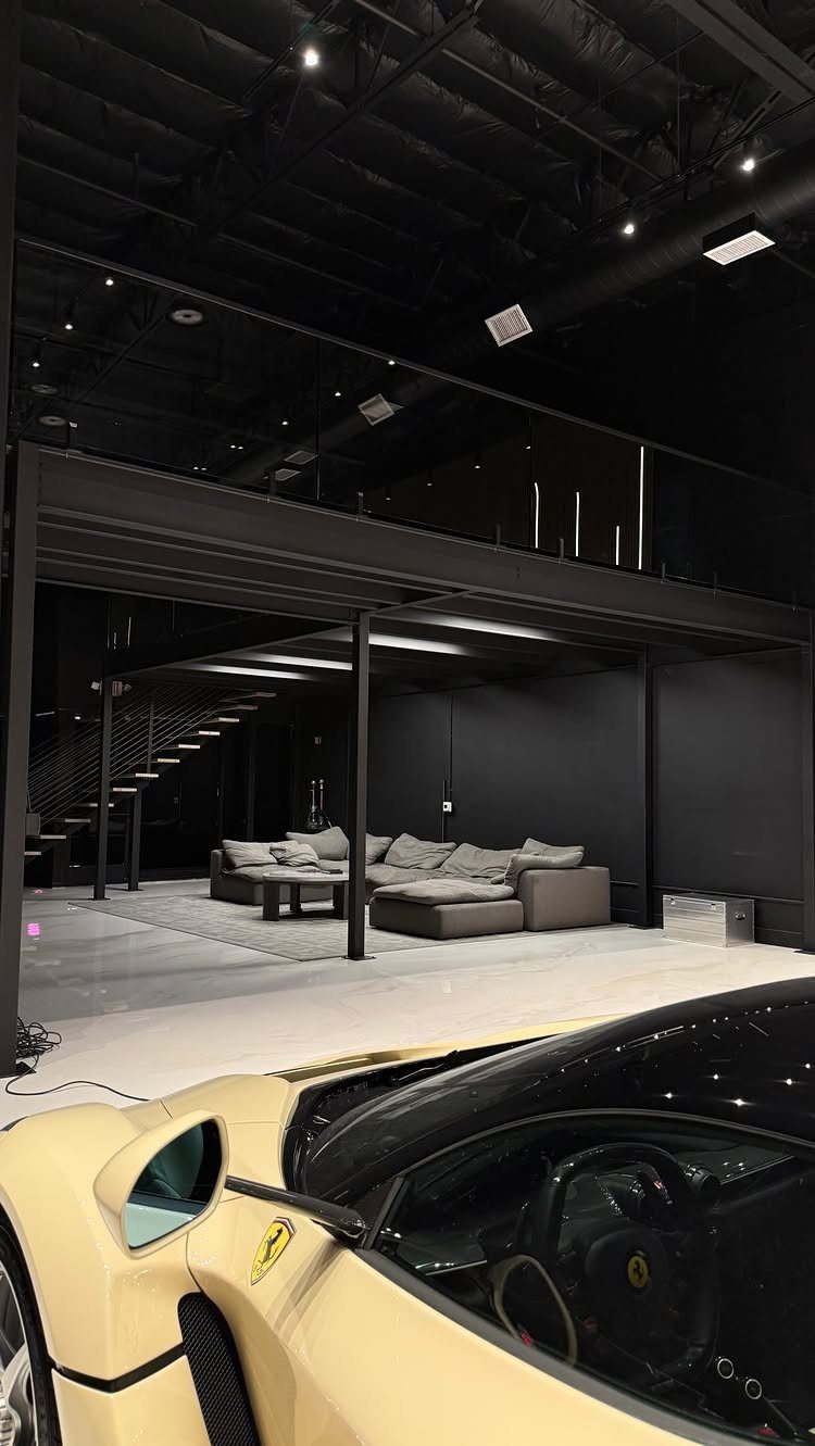 Modern dark garage with a luxury sofa and a mezzanine loft featuring a glass railing.