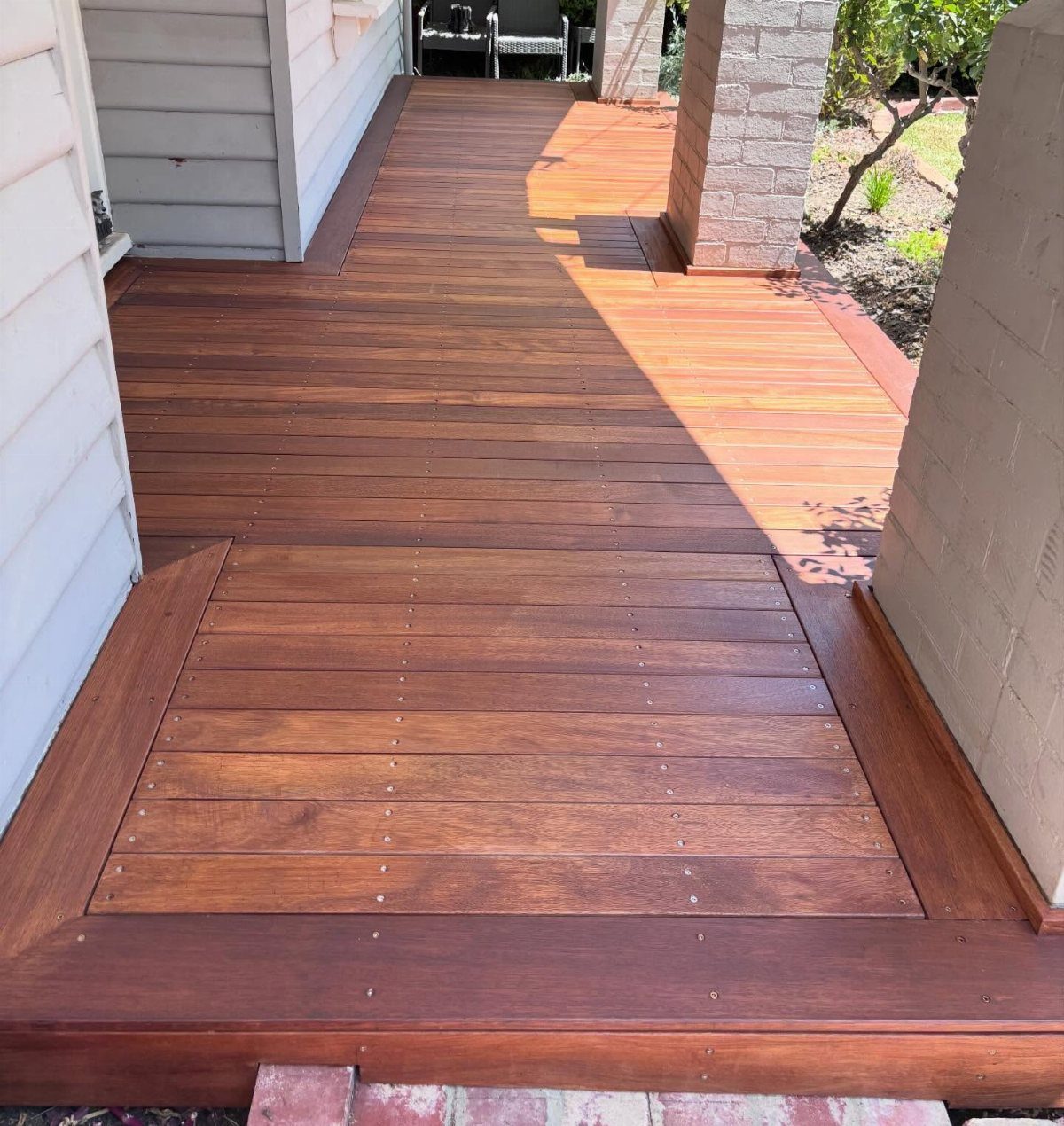 Polished reddish-brown wooden deck with decorative rectangular plank inlay patterns next to a house.
