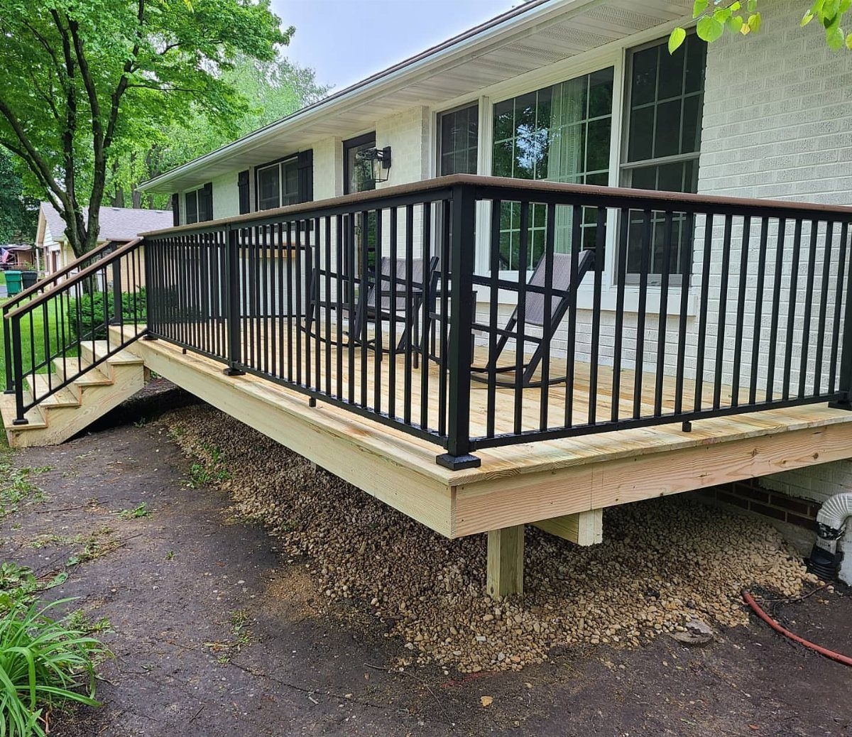A wooden raised deck with black metal railings and dark brown drink rail caps attached to a white house.