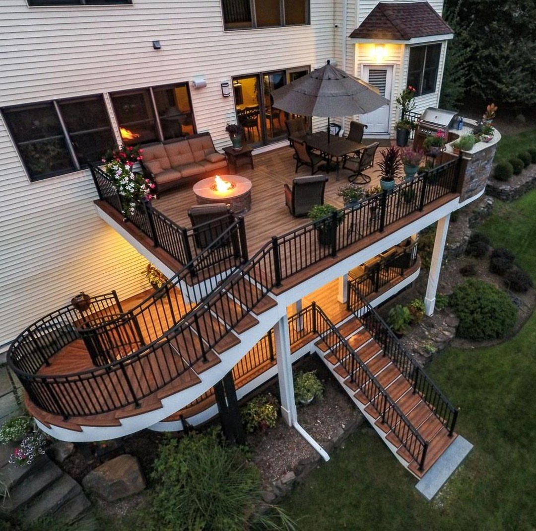 A multi-level wooden deck with curved stairs, outdoor furniture, and a fire pit attached to a house.