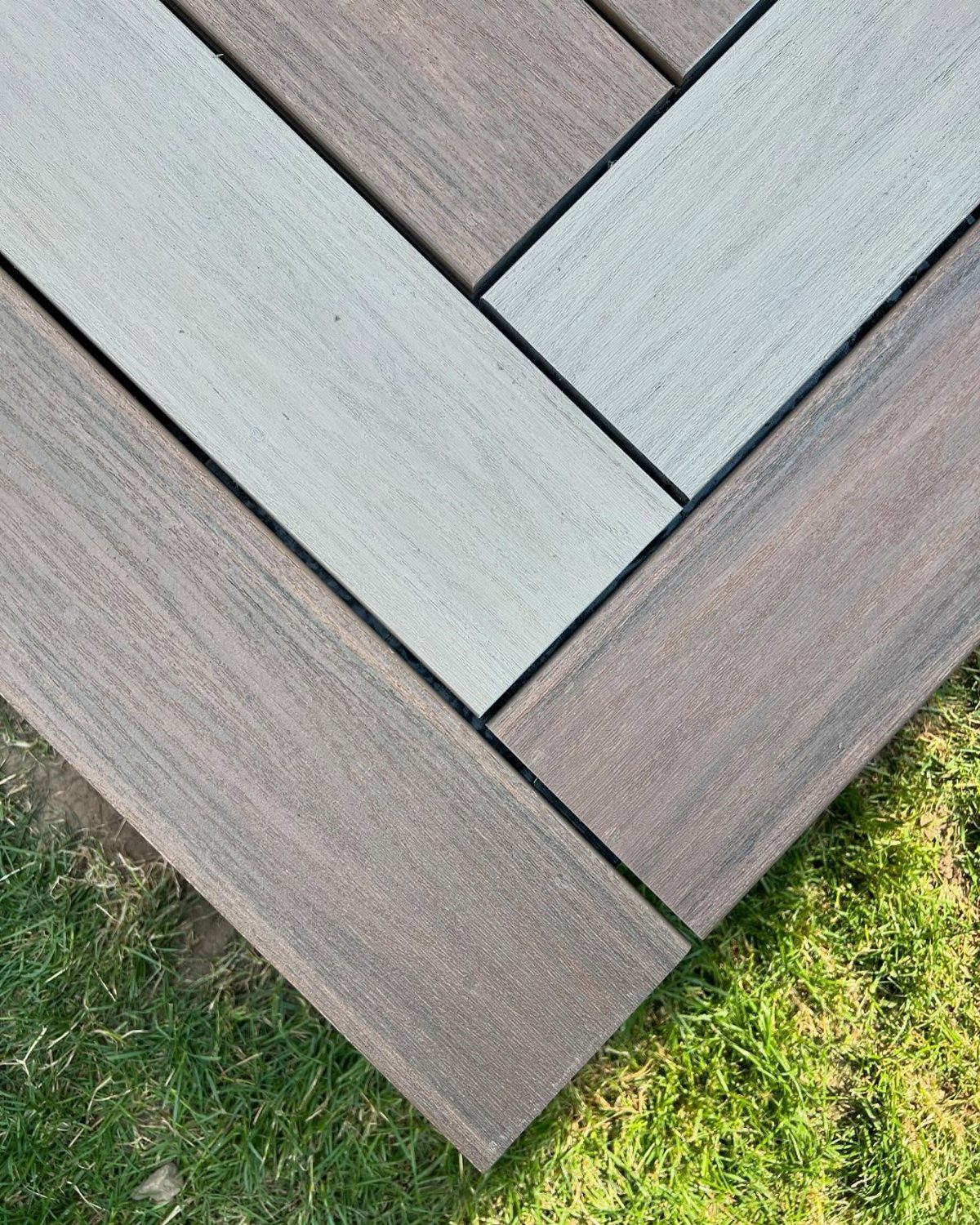 Diagonal composite decking boards in grey and brown colors meeting at a corner edge.