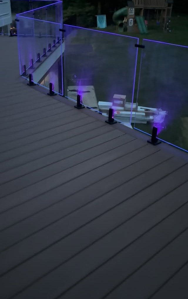 Glass railing with purple LED lighting installed on a dark wooden deck at night.