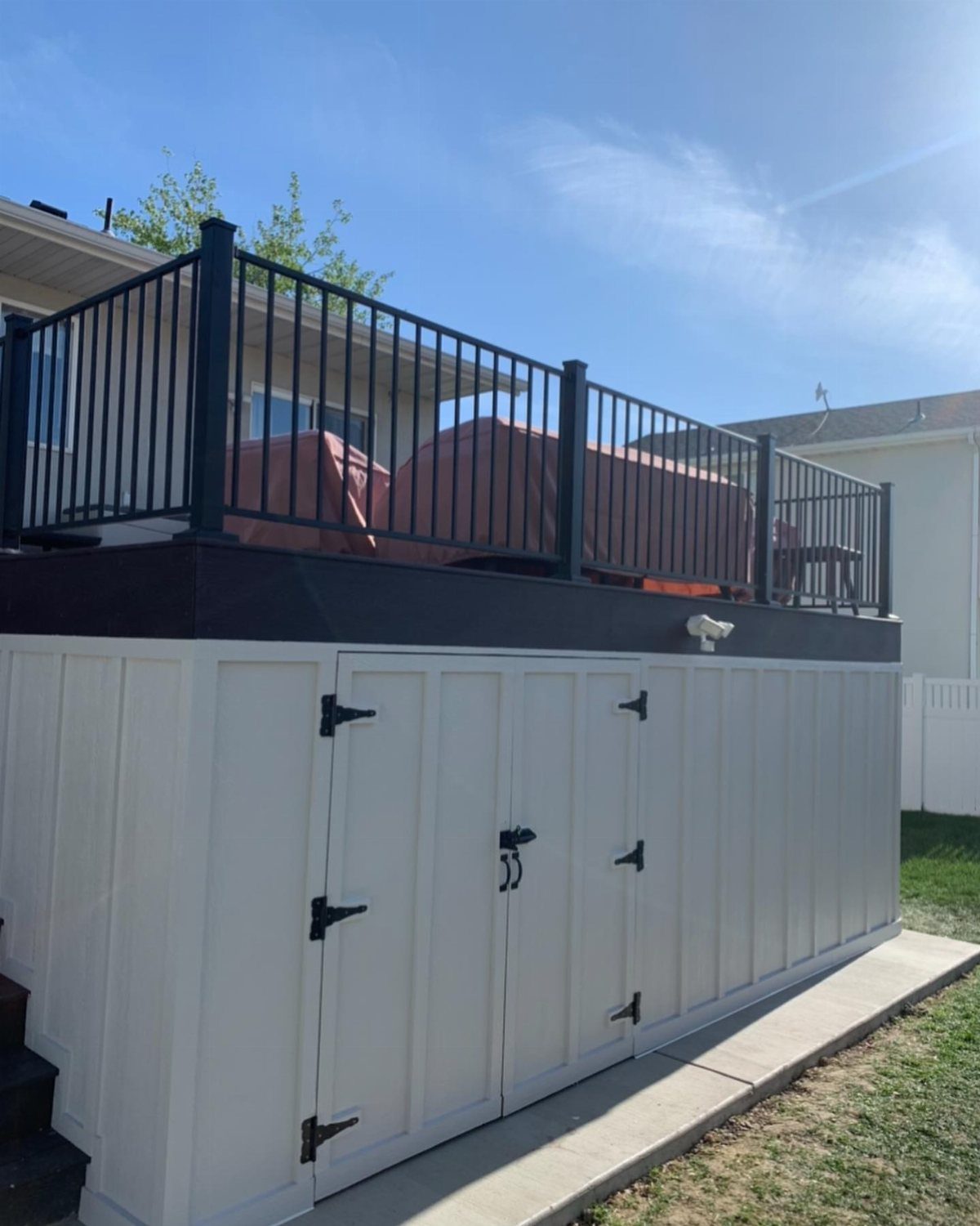 White storage cabinets with black hinges built underneath a dark raised wooden deck.