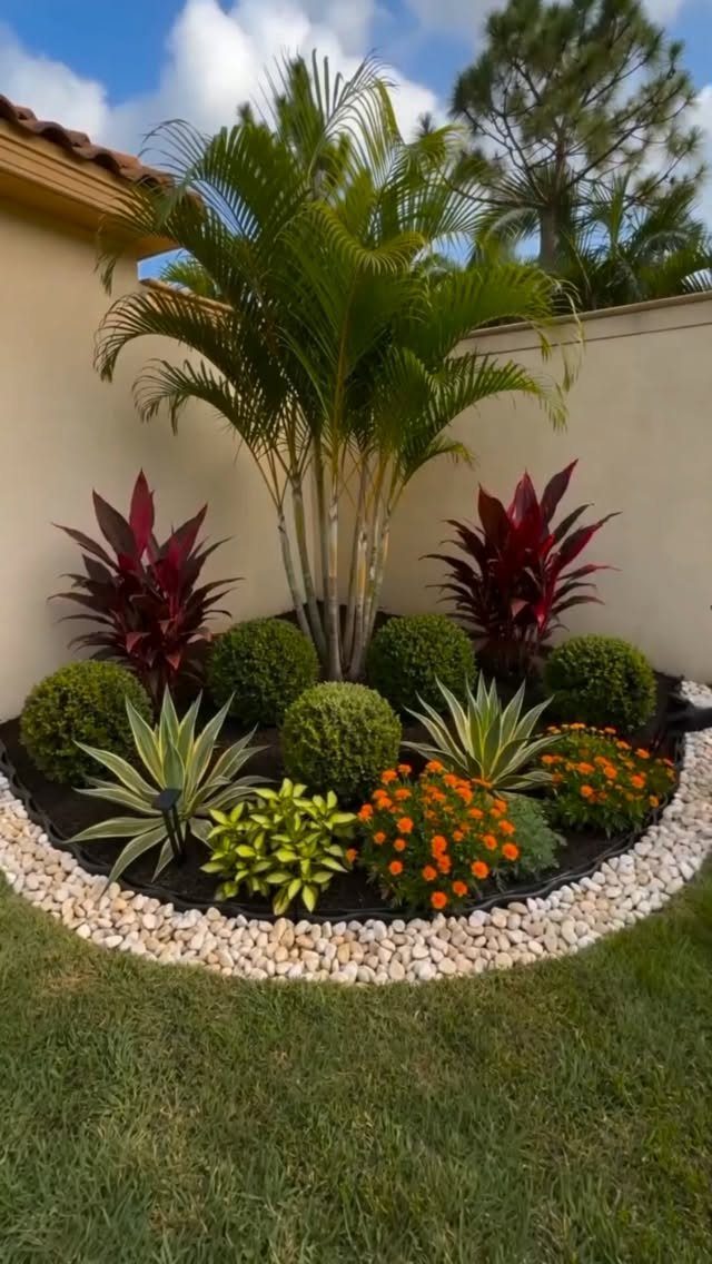 Simple Garden Layout Ideas for 2026: 12 Plans to Try 12 A tropical garden bed with a palm tree, red plants, and orange flowers surrounded by white pebbles.
