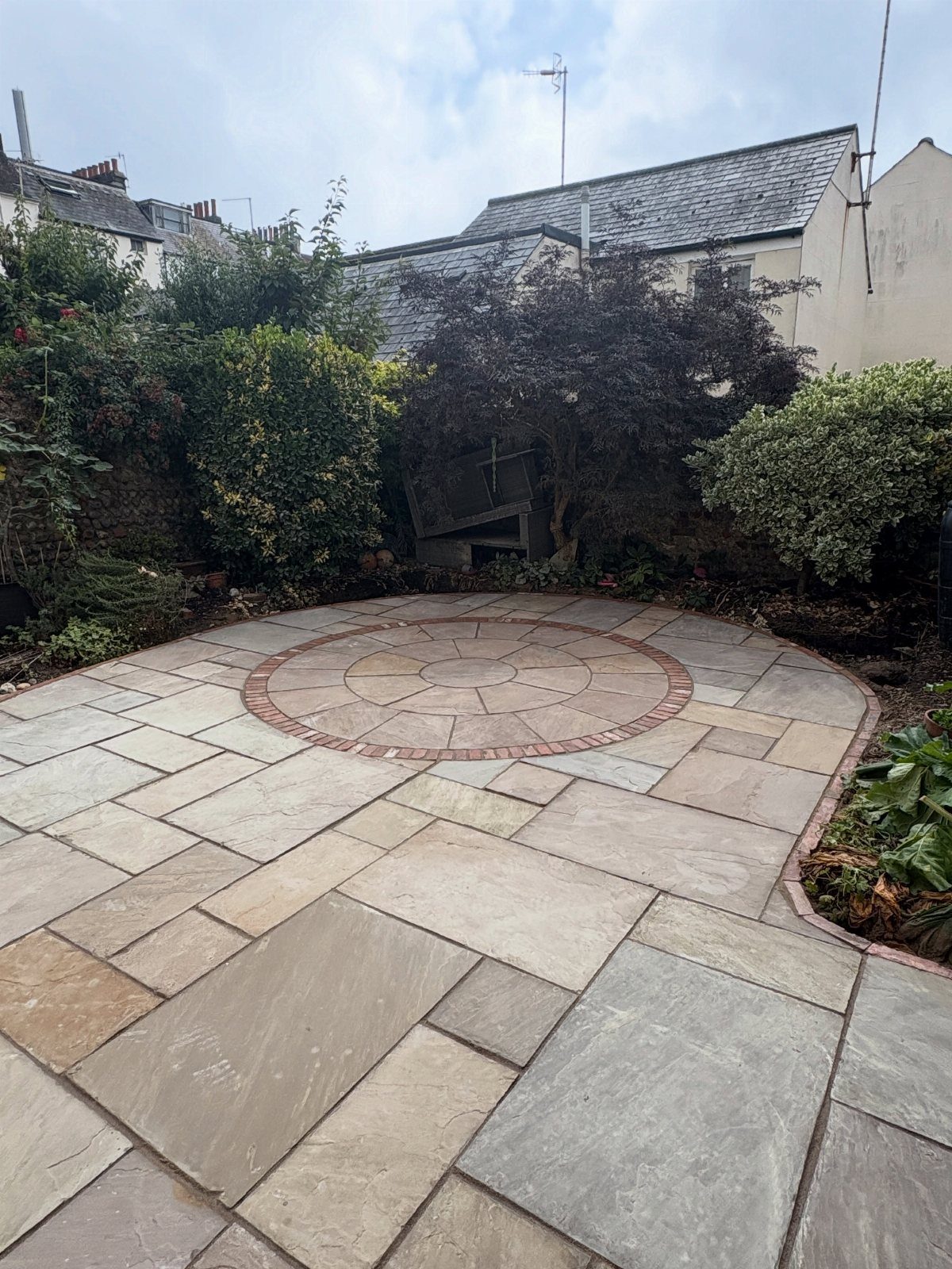 7 Small Yard Garden Ideas for Edibles, Patios and Seating 4 A flagstone patio with a circular stone pattern and brick border in a small garden.