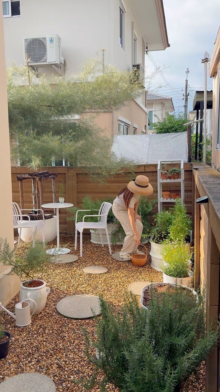 7 Small Yard Garden Ideas for Edibles, Patios and Seating 6 A woman tending to various green plants in white pots within a small gravel courtyard garden.