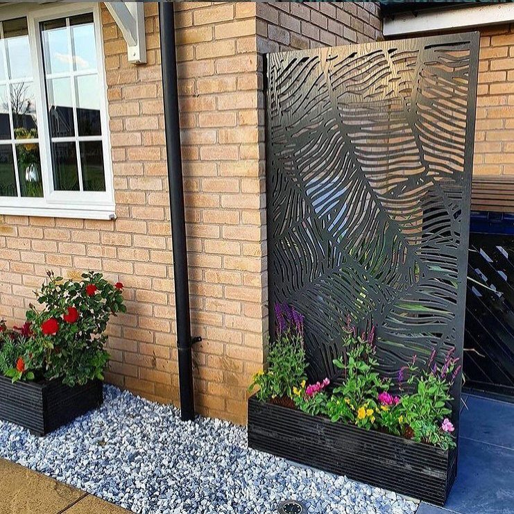 13 Unique Garden Ideas for Planters, Privacy Screens and Pallet Projects 1 A decorative metal privacy screen with leaf cutouts and a flower planter against a brick wall.
