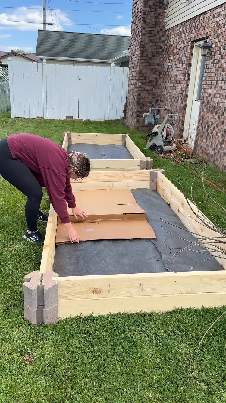A person placing cardboard into a wooden raised garden bed lined with fabric.