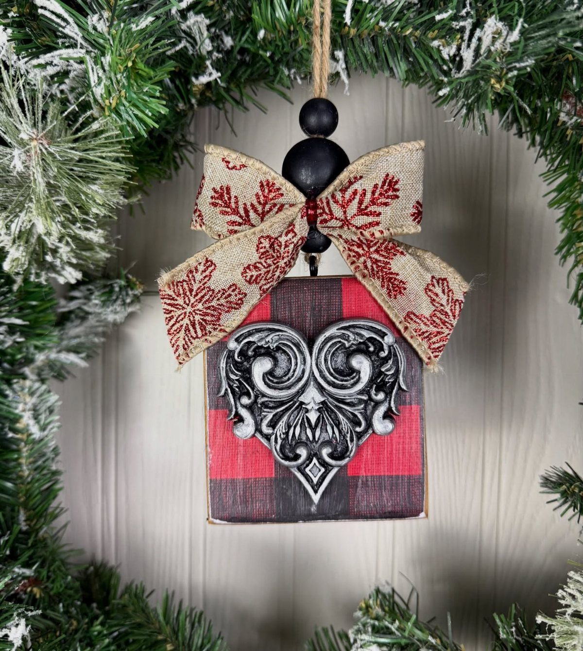 Hand-painted wooden block ornament with red plaid and silver scrollwork heart hanging in a wreath.