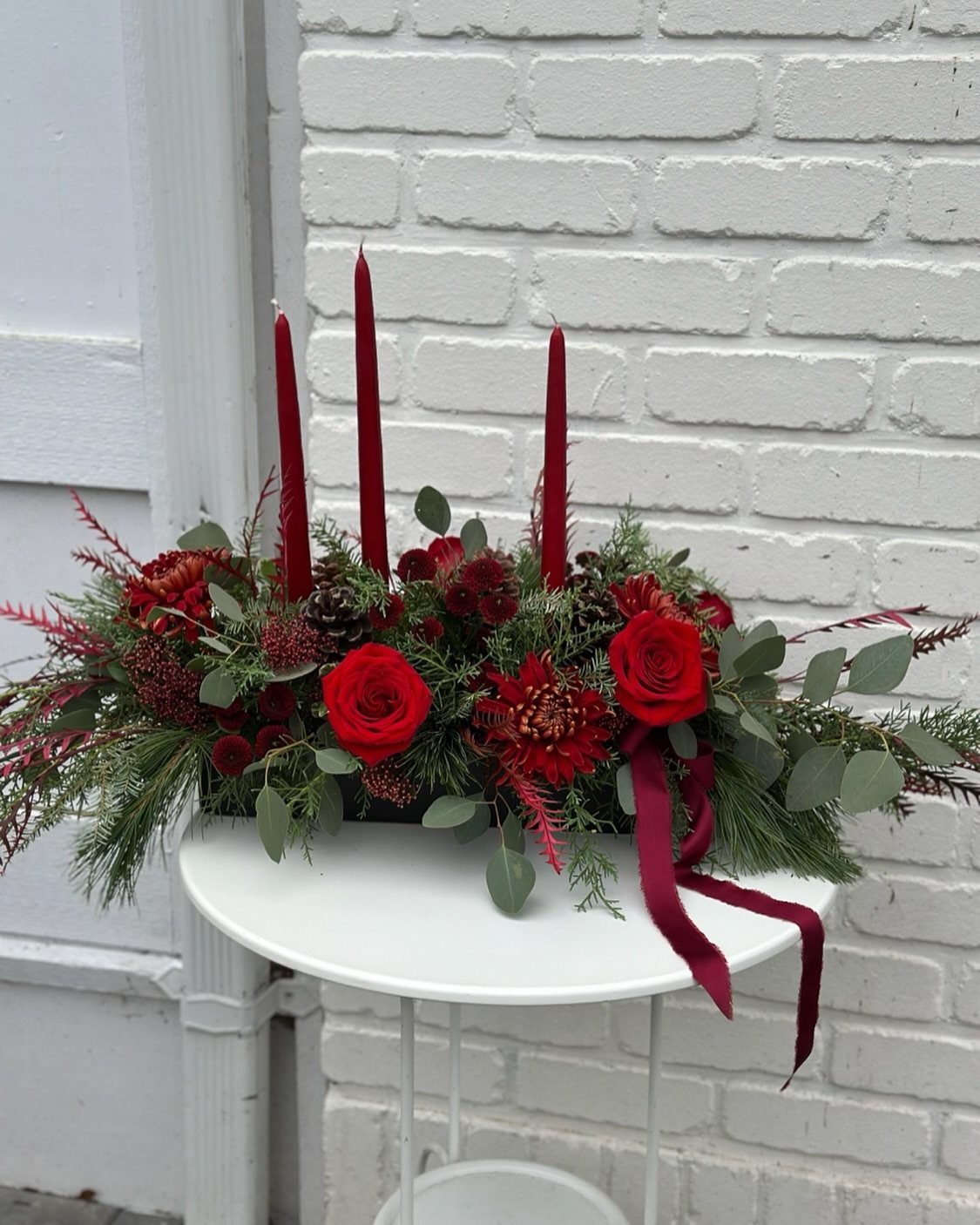 12 Xmas Table Decorations for Pine Cones, Mercury Glass, and Blue-Gold Palettes 3 Red roses and taper candles arranged with greenery and berries on a white table.